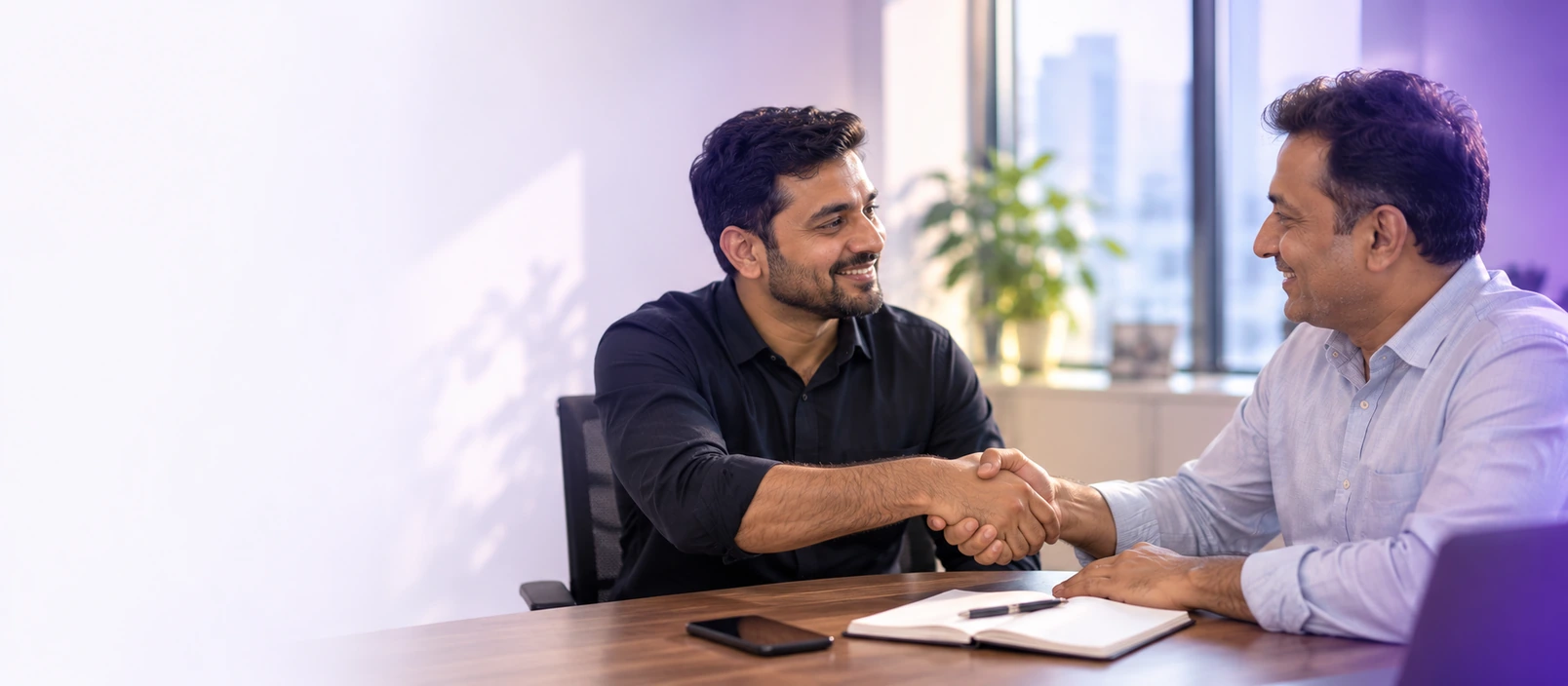 Two business owners shaking hands across a table in an Ahmedabad office.
